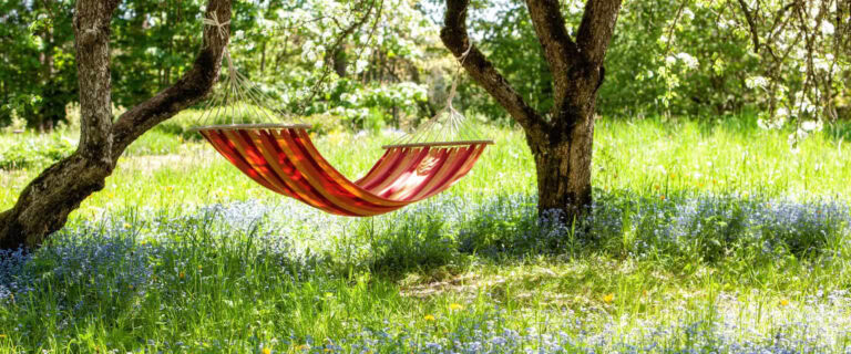 Schöne Landschaft mit roter Hängematte im Frühlingsgarten